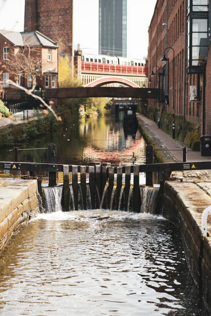 pexels-photo-7455499-7455499-1 Charming canal scene in Manchester with bridges and historic architecture reflecting urban charm.